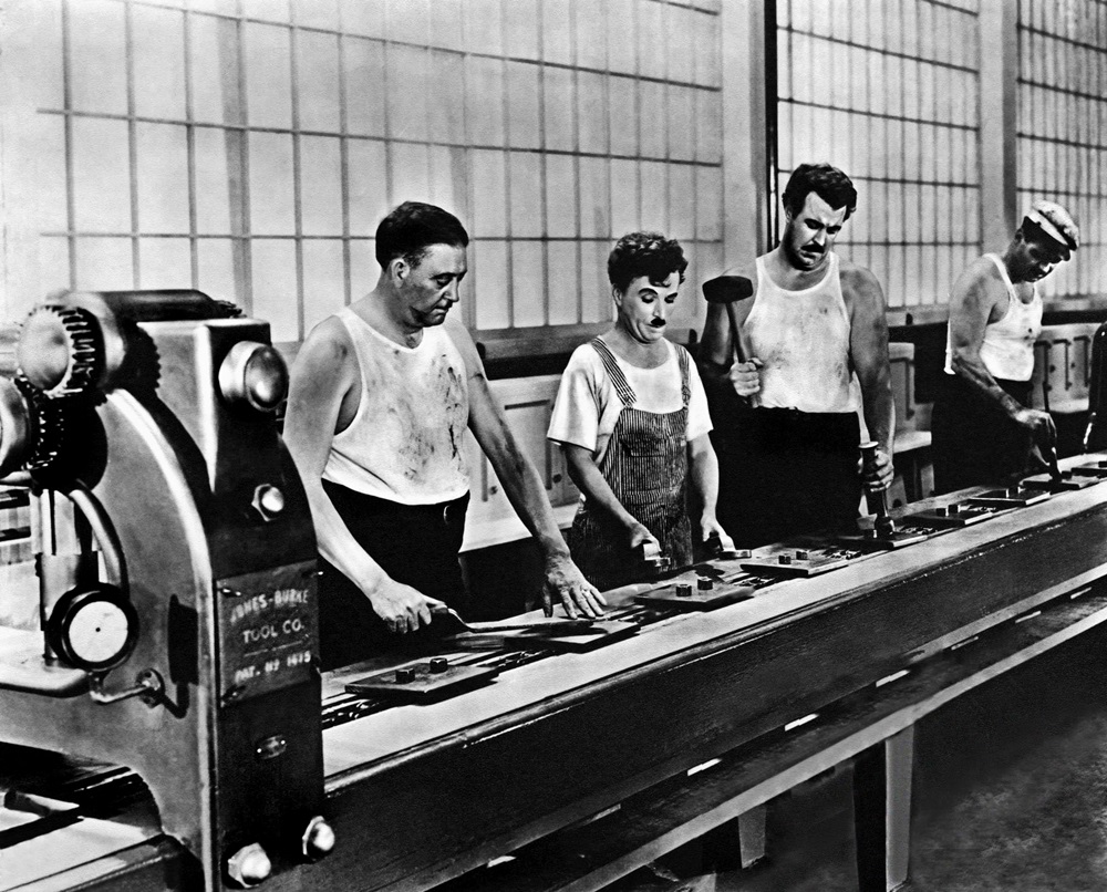 Charlie Chaplin (tweede van links) aan delopende band in Modern Times, 1936.