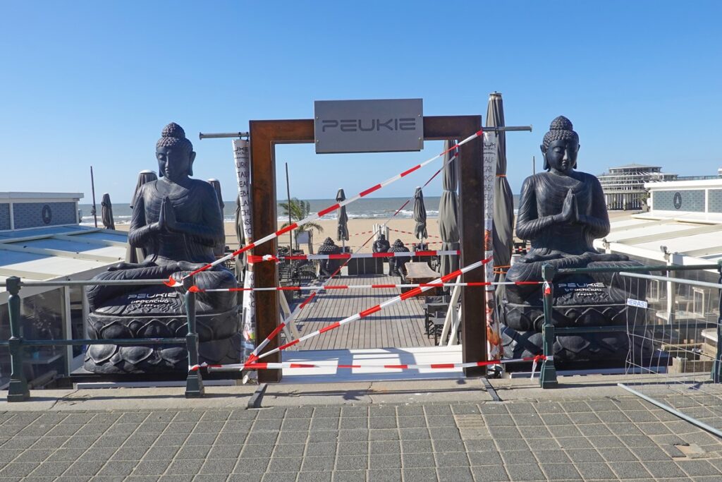 Boeddha’s flankeren de ingang van strandtentPeukie in Scheveningen, die is afgezet
vanwege de corona-epidemie,
31 maart 2020.